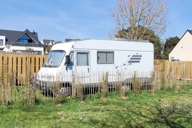 Un camping-car sur un emplacement en herbe, entouré de palissades en bois et d’une ganivelle