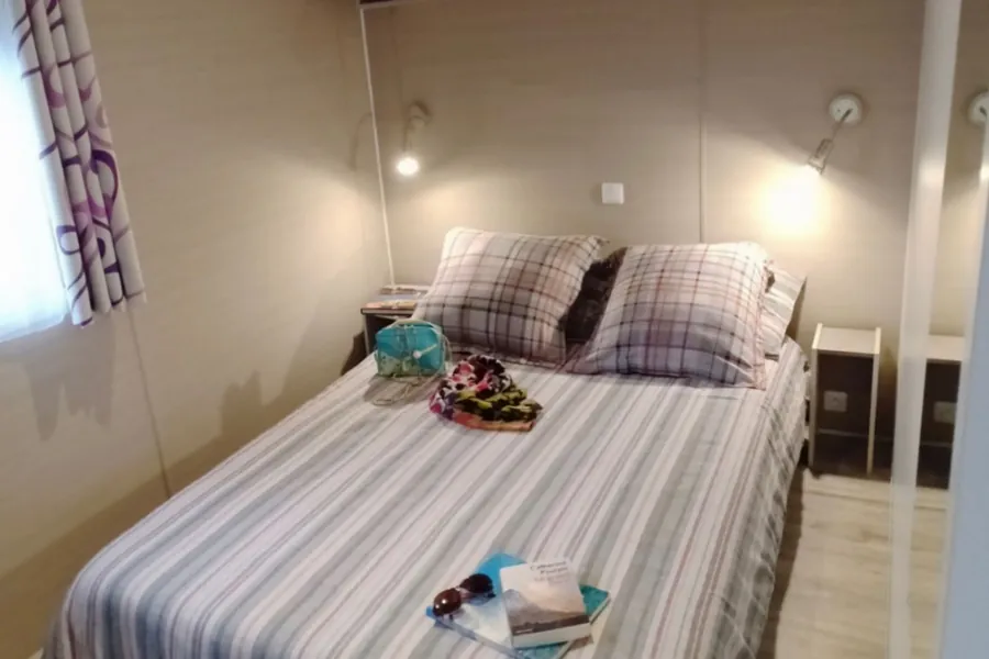 La chambre parentale du mobil-home Belle-Île : un lit double, des coussins à carreaux, deux liseuses murales et deux chevets