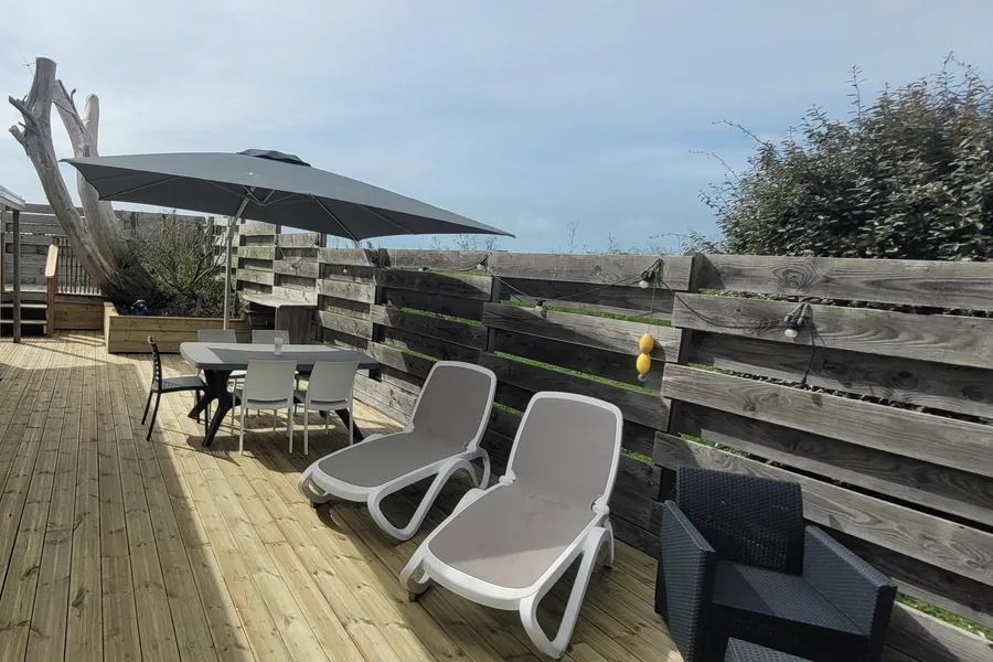 La terrasse en bois du mobil-home Sunset, avec transats, table, parasol et palissade