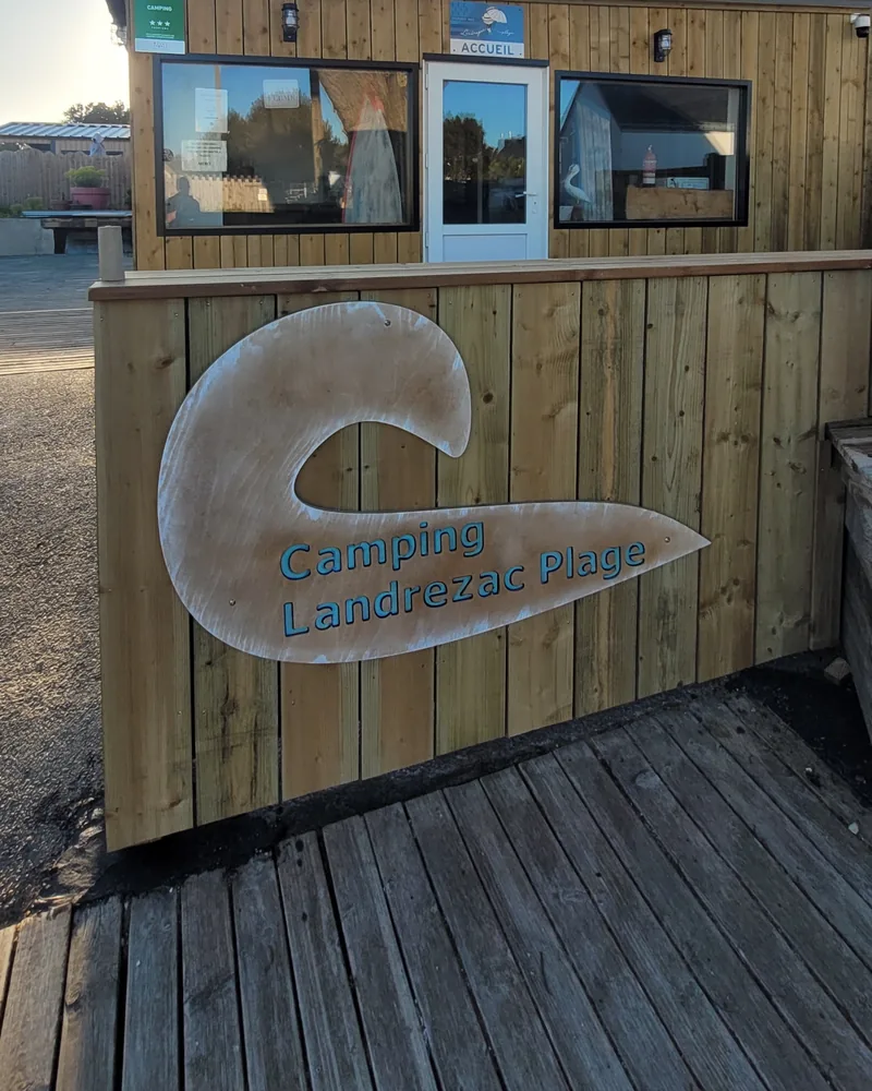 Le bâtiment de l’accueil, en bois, avec le logo du Camping Landrezac Plage