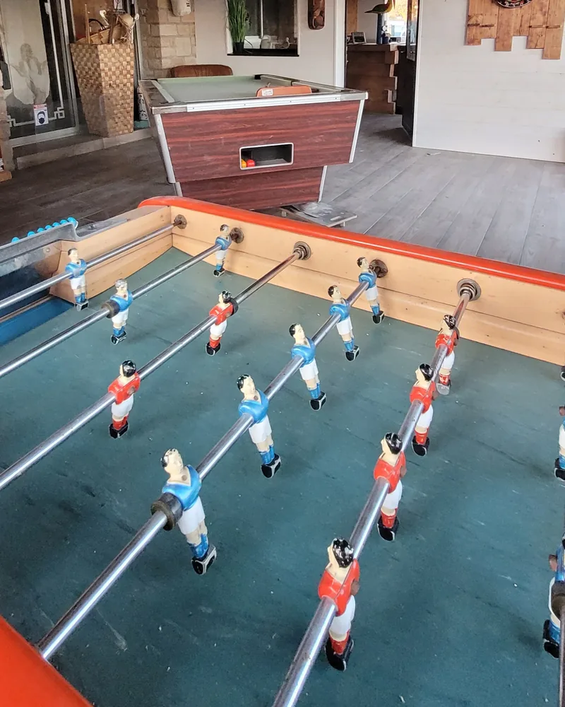 Un baby-foot au premier plan et un billard dans la salle de jeux, des planches de paddle fixées au plafond