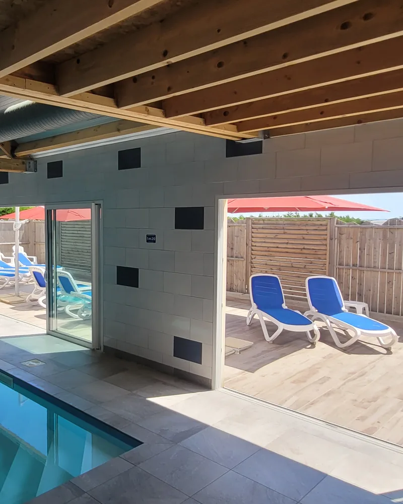 Les baies vitrées de la piscine intérieure, ouvertes sur une terrasse avec des transats bleus
