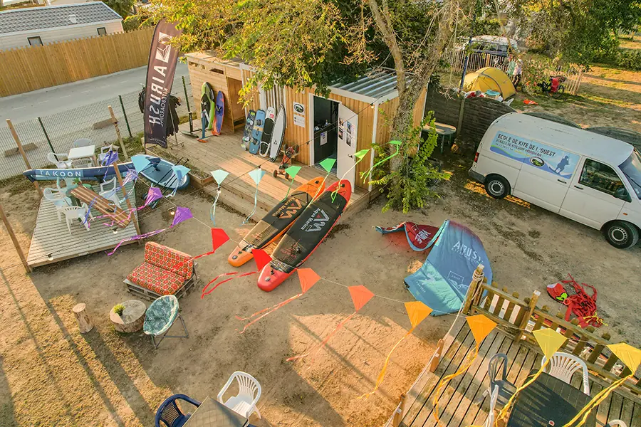 Vu d’en haut : le chalet de l’école EKO Kite, ses planches de paddle et de kitesurf posées sur le sable, des fanions et le camion de l’école