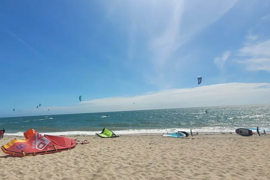 Une dizaine d’ailes de kitesurf dans le ciel au-dessus de la mer, à Landrezac ; au premier plan, des ailes posées sur le sable